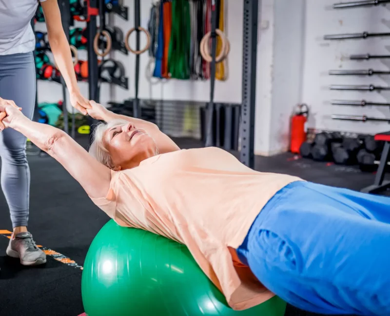 senior-woman-with-trainer-doing-rehab-using-pilate-2023-11-27-05-01-47-utc@2x